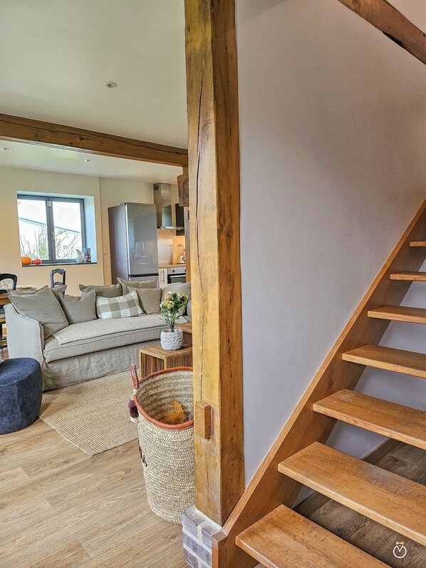 A staircase with wooden steps leading to a landing, a sofa, a small table with a vase, and a window with a view of the outdoors.