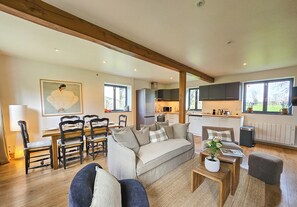 Un grand espace de vie comprenant un canapé, des fauteuils, une table à manger et une cuisine à l’arrière-plan.