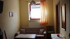 A room with a sofa, a table, a chair, a window with curtains, and a radiator. - 3. standard double room (Lena) in a quiet location in Görlitz (Görlitz)