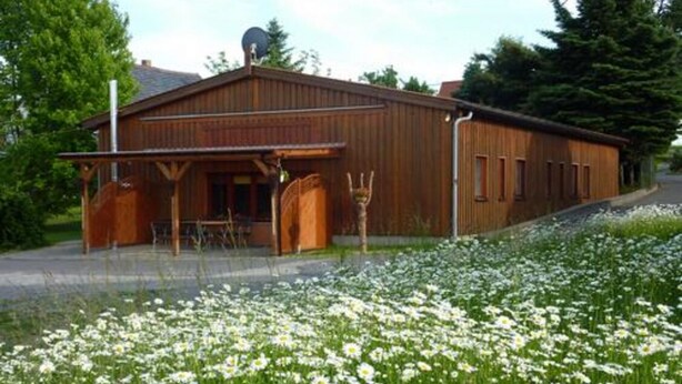 A wooden building with a porch, a satellite dish, and a garden with white flowers. - 3. standard double room (Lena) in a quiet location in Görlitz (Görlitz)