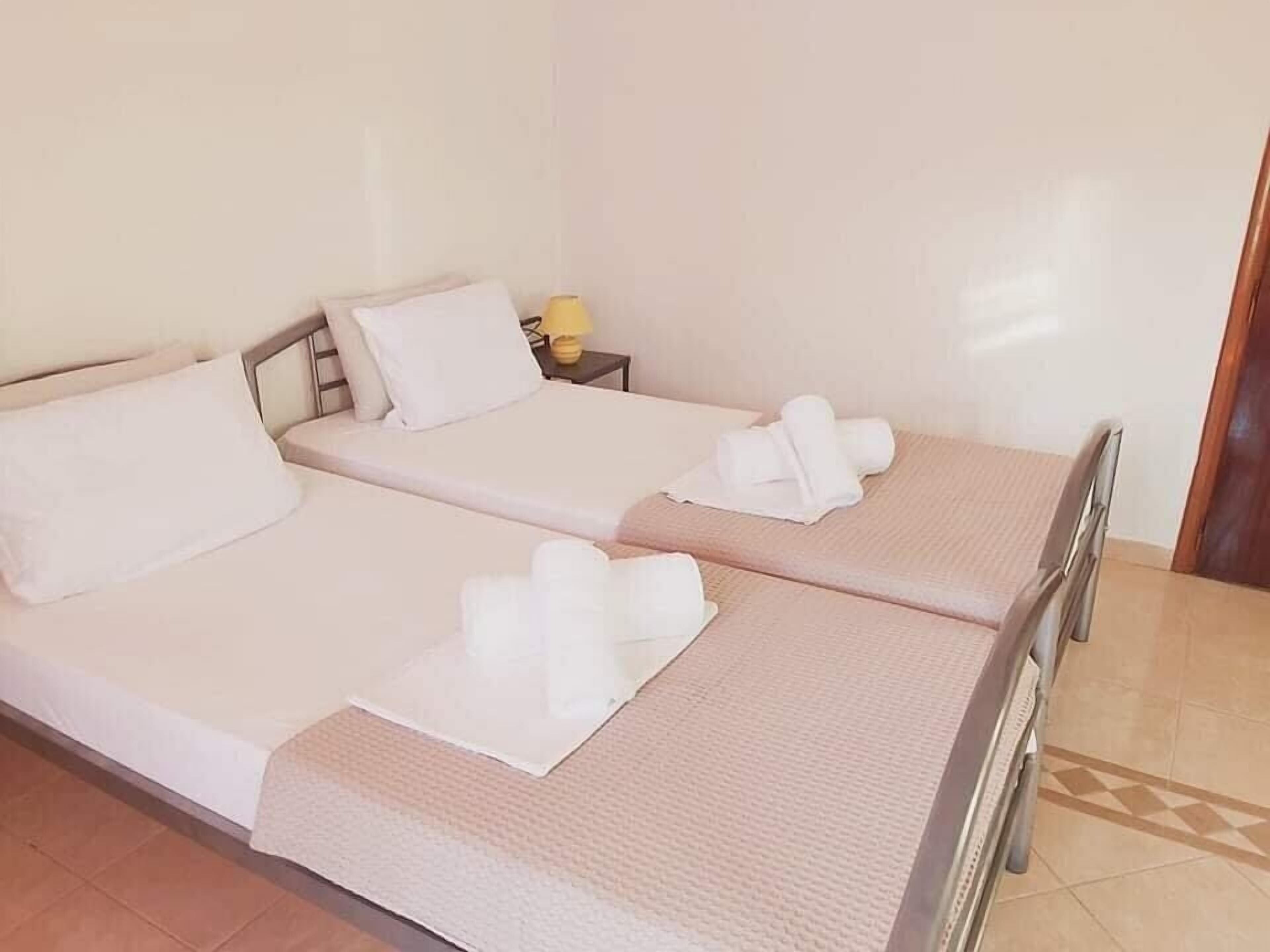 Habitación de hotel con dos camas, cada una con un almohadón blanco y toallas enrolladas.