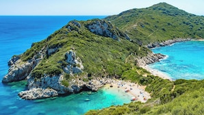 Un paysage côtier avec une île rocheuse, des eaux turquoise et limpides, et une plage où se trouvent des gens.
