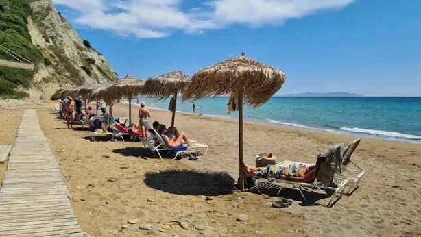 Une plage avec des parasols en chaume et des chaises longues, le tout bordant une promenade en bois.