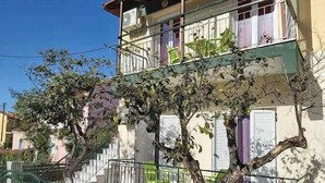 Un edifici de diversos pisos amb balcons, una escala i un arbre al primer pla.
