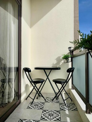 Un petit balcon doté d’un sol carrelé, de deux chaises pliantes et d’une table.