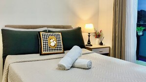 Hotellihuone, jossa on sänky, yöpöytä, lamppu, ikkuna verhoilla ja näkymä ulos.