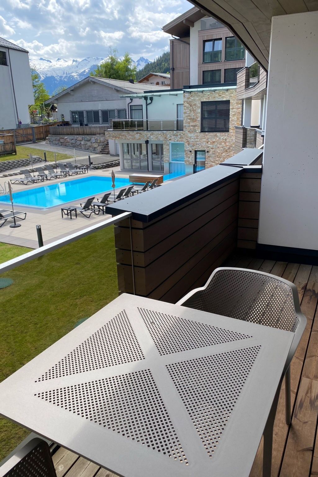 Un balcón con vista a la piscina, una mesa con diseño perforado y vistas a la montaña.
