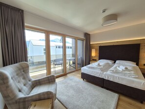 A hotel room with a bed, a chair, a small table, and a view through large windows. - 3_SPA - Deluxe Panorama 522 by Interhome (Zell am See)