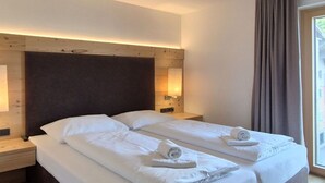 Ein Doppelbett mit weißen Laken, ein Kopfteil, Nachttischlampen und ein Fenster mit Vorhängen.
