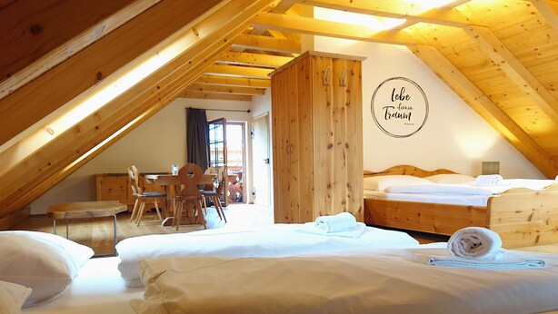 A cozy attic bedroom with wooden beams, a dining area, and a bed with neatly made linens. - 6_ALP - Hochgolling 1  - Loft Apartment by Interhome (Mariapfarr)