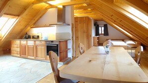 An attic bedroom with a wooden ceiling, a dining table, and a kitchenette. - 6_ALP - Hochgolling 1  - Loft Apartment by Interhome (Mariapfarr)