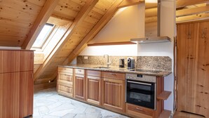 A modern kitchen with wooden cabinets, a granite countertop, and a built-in oven. - 6_ALP - Hochgolling 1  - Loft Apartment by Interhome (Mariapfarr)