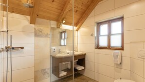 A bathroom with a shower, sink, and toilet, wooden ceiling, and a window. - 6_ALP - Hochgolling 1  - Loft Apartment by Interhome (Mariapfarr)