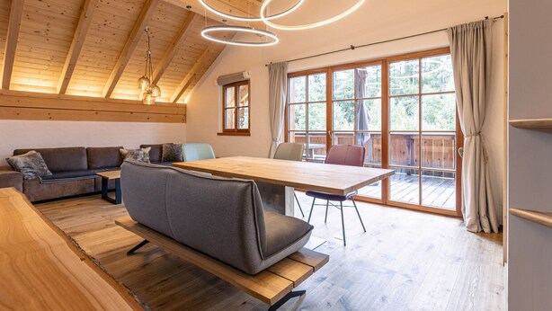 A modern interior with a wooden ceiling, a dining table, a sofa, and a large window with curtains. - 6_ALP - Penthouse Preber by Interhome (Mariapfarr)