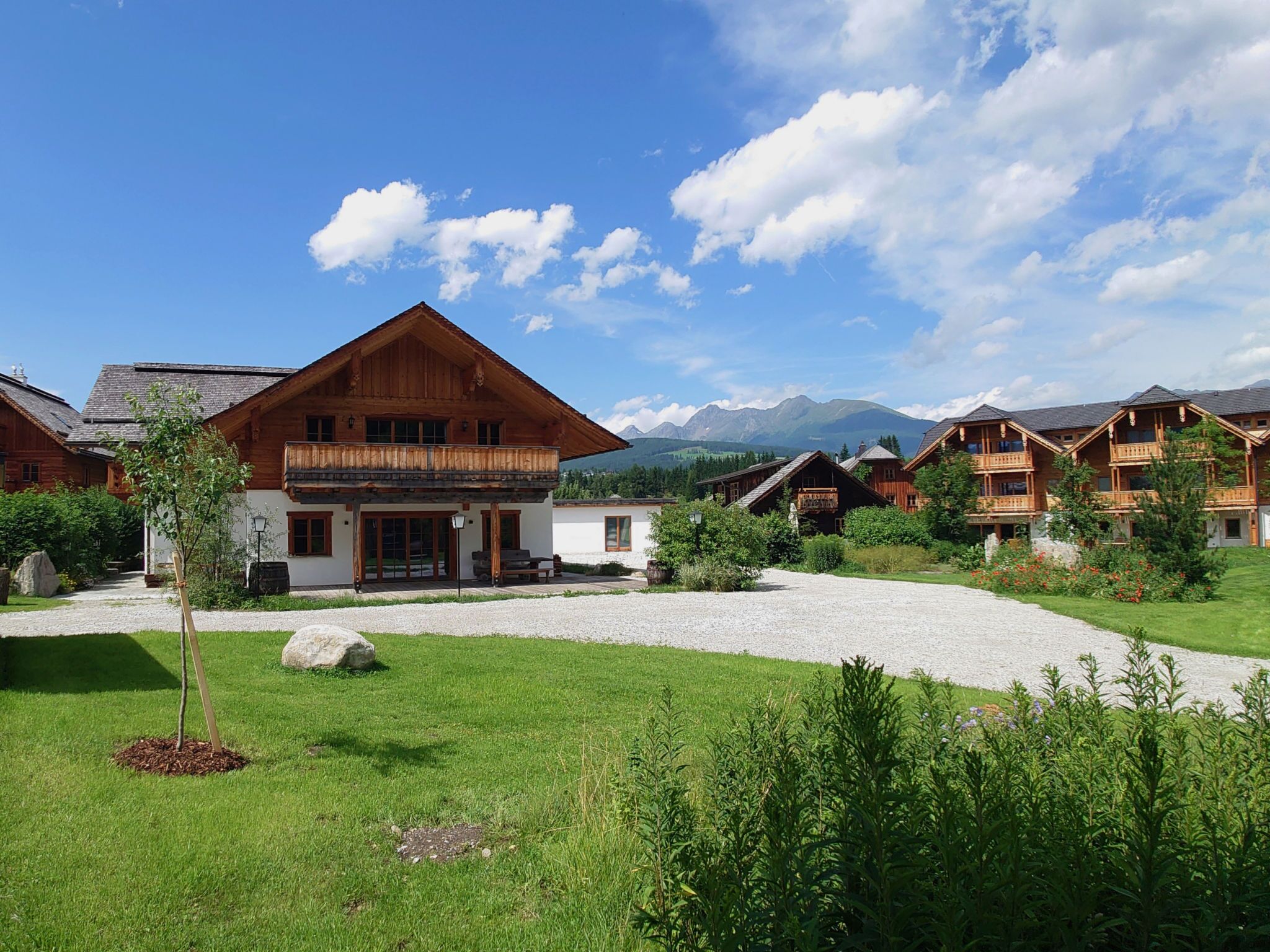 Ein Chalet-Hotel mit großer Holzfassade, einem Schotterweg und einem Bergpanorama im Hintergrund.