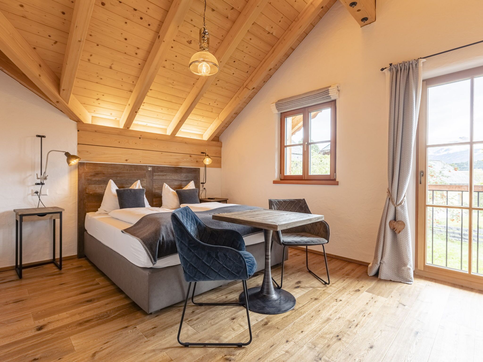 Une chambre à coucher comprenant un lit, une table, des chaises, une lampe, une fenêtre et une vue sur l’extérieur.