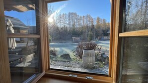 Ett fönster med utsikt över en innergård, en träbänk och en planteringslåda i sten.