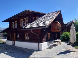 Una cabaña de madera con techo inclinado, un patio de piedra y mobiliario de exterior.