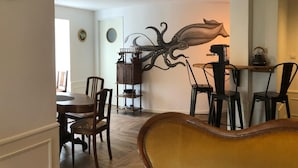 Uma área de refeições com mesa e cadeiras de madeira, arte decorativa de polvo na parede e uma chaleira preta em uma prateleira.