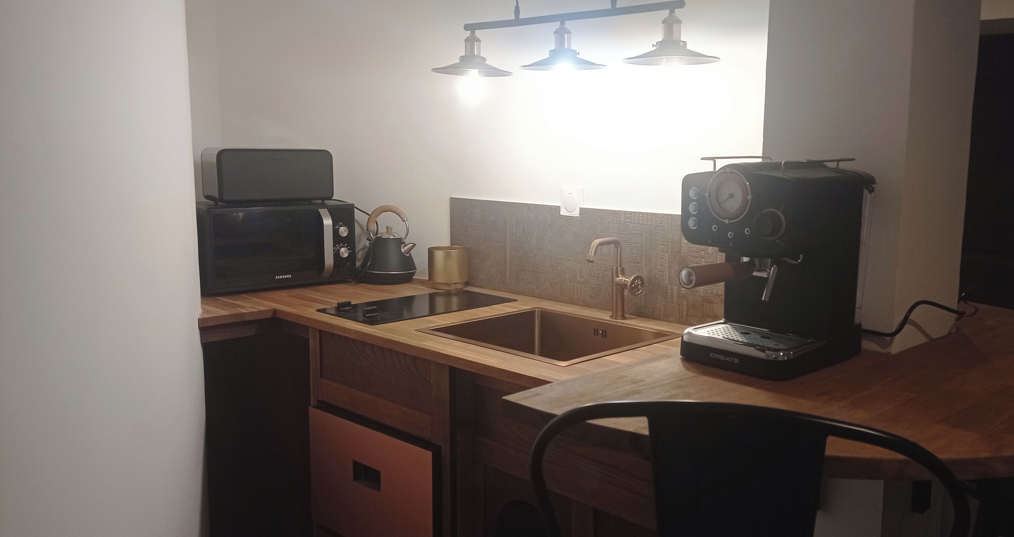 A compact kitchen with a microwave, kettle, coffee maker, and a sink.