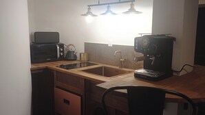 Uma cozinha compacta com micro-ondas, chaleira, máquina de café e pia.