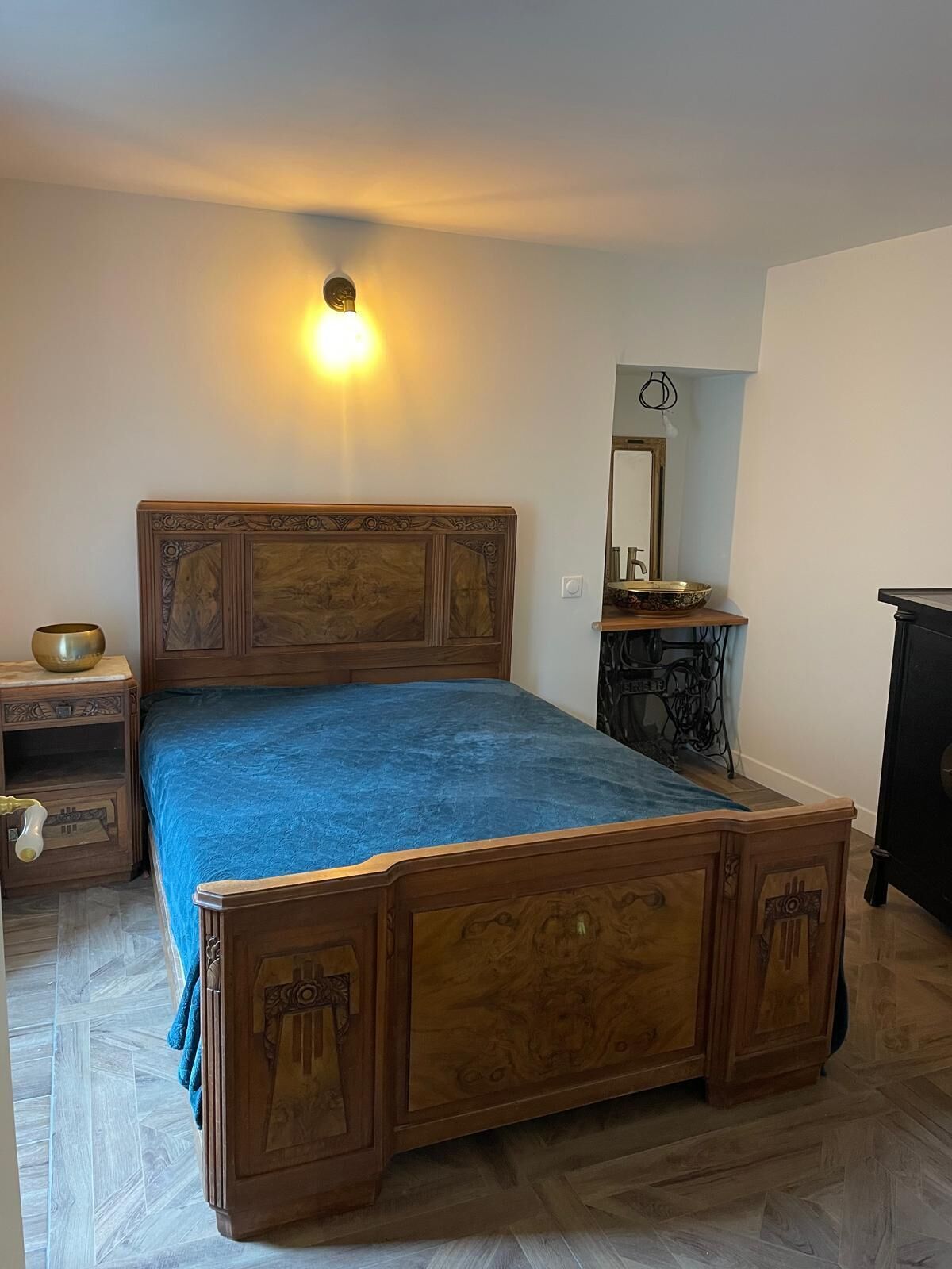 A bedroom with a wooden bed, a bedside table, a lamp, a mirror, and a dresser.