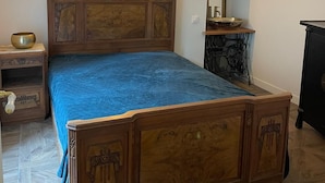 Quarto com cama de madeira, mesa de cabeceira, luminária, espelho e cômoda.