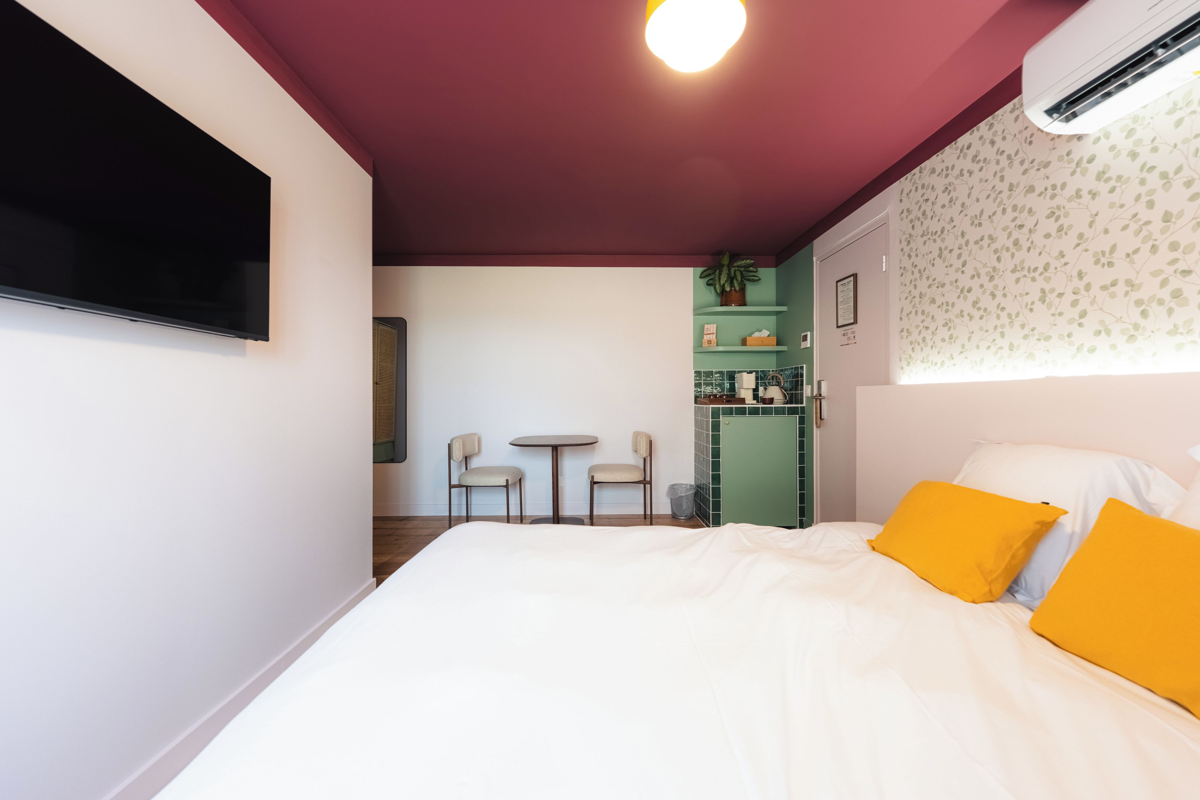 A hotel room with a bed, a TV, a desk with chairs, a kitchenette, and a bathroom.