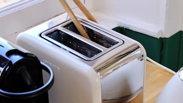 A kitchen with a toaster on a wooden table, a black object on the left, and a window in the background.