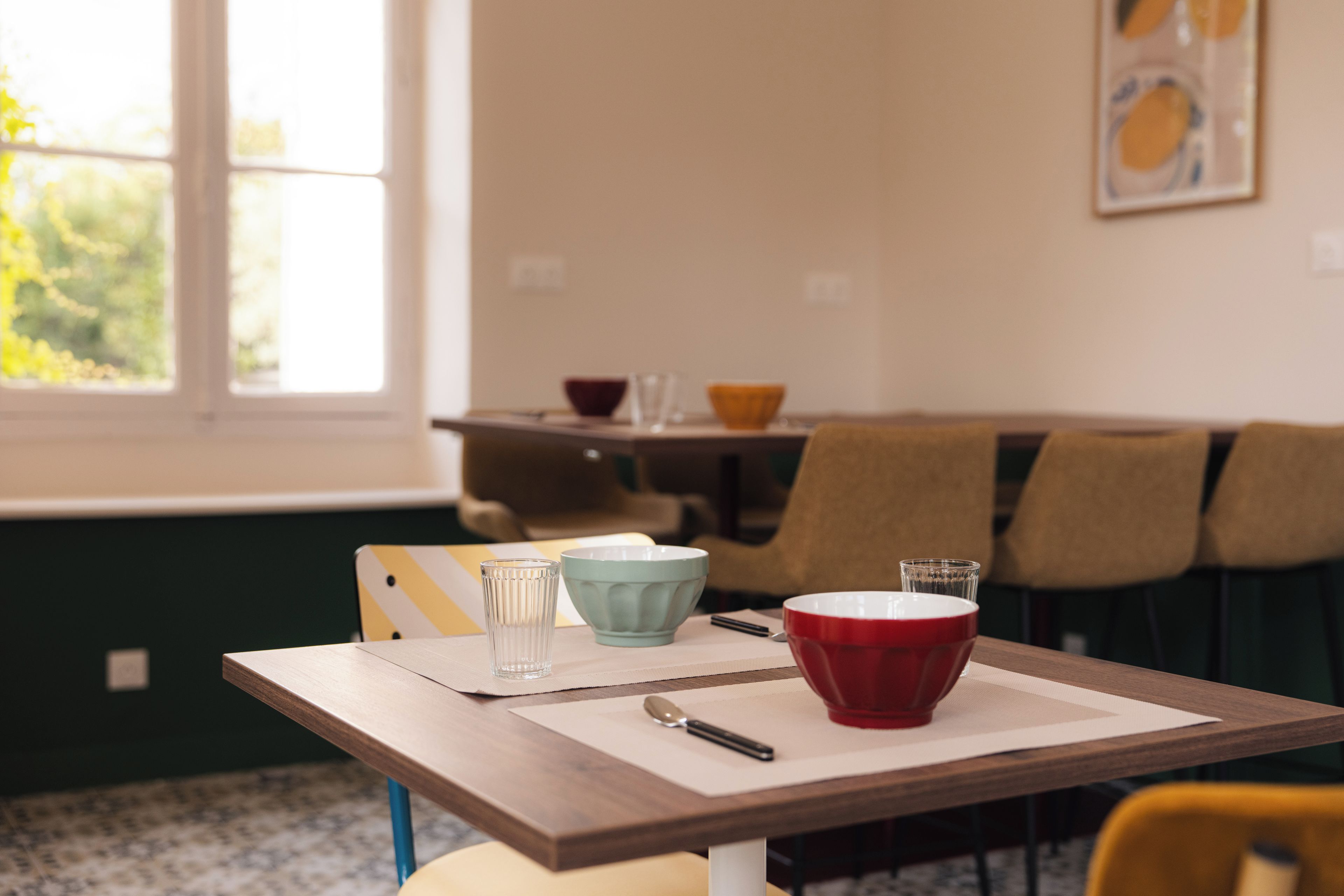 Een eettafel met een placemat, een rode kom, een helder glas en een lepel.