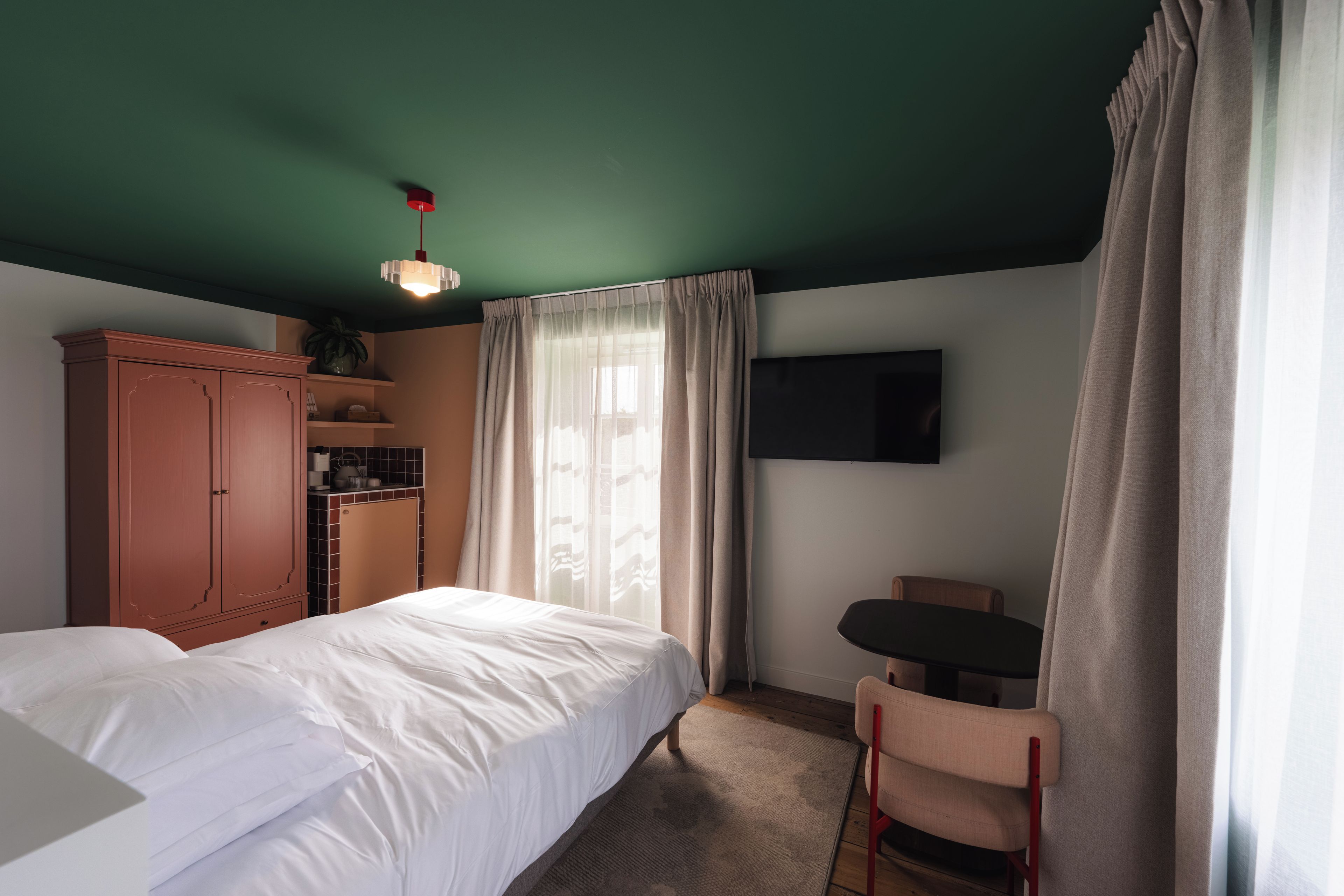 A hotel room with a bed, a desk, a chair, a television, and a wardrobe.