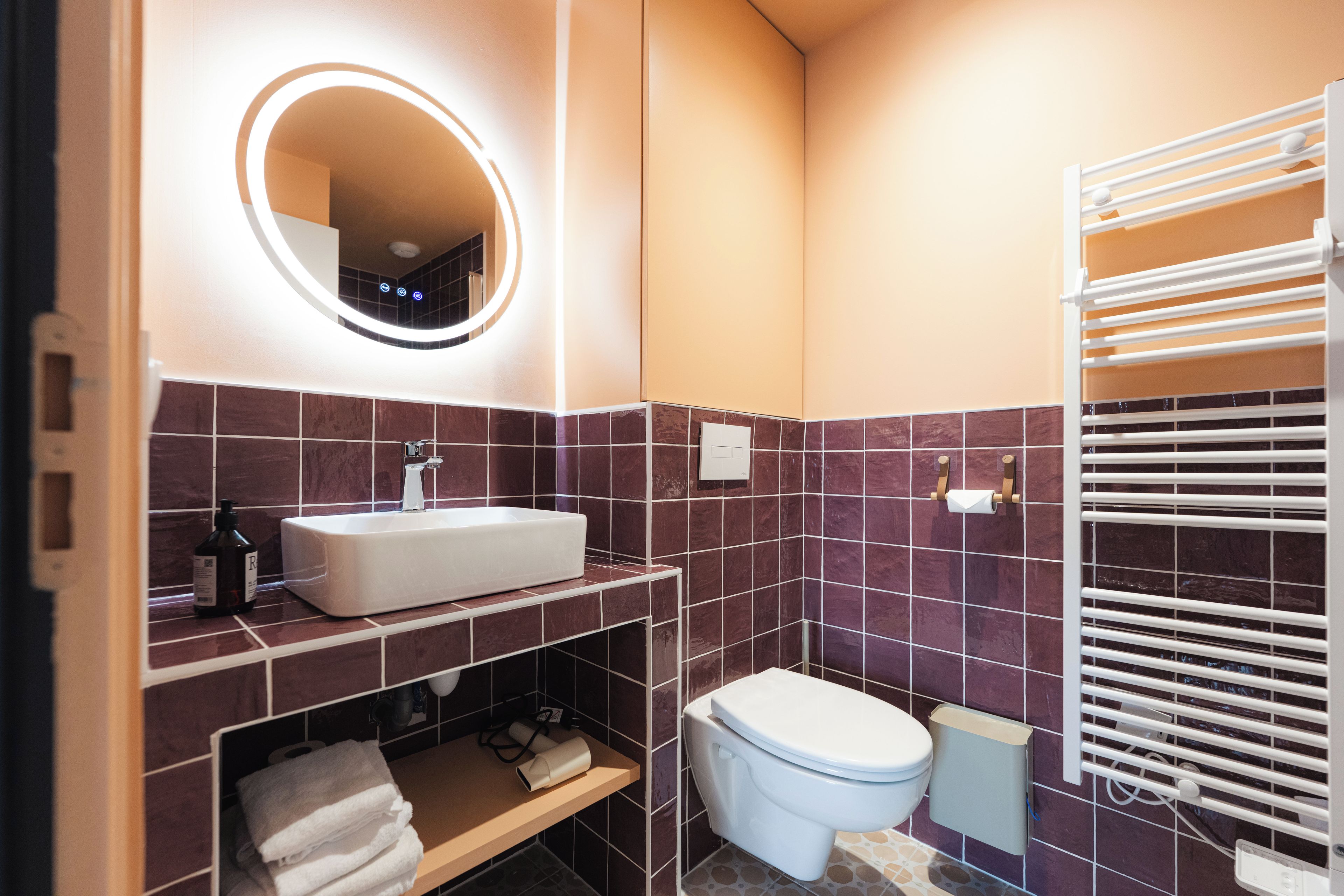 Un baño moderno con un lavamanos blanco, un espejo, un inodoro y un perchero para toallas.