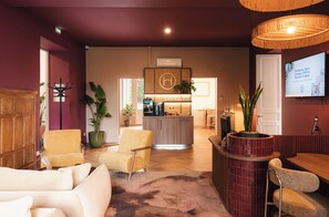 A hotel lobby with seating, a reception desk, and a television displaying a wine region. - Héméra Cognac (Cognac)