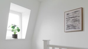 A staircase with white railings, a small window with a plant, and a framed artwork on the wall. - Hampstead Heath 2 bed (Greater London)