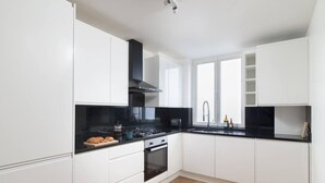 A modern kitchen with white cabinetry, a black countertop, and a wooden floor. - Hampstead Heath 2 bed (Greater London)