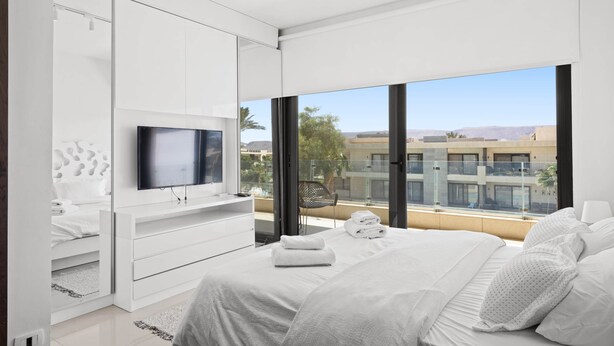 Un dormitorio moderno con una cama, un televisor y vistas a la ciudad.