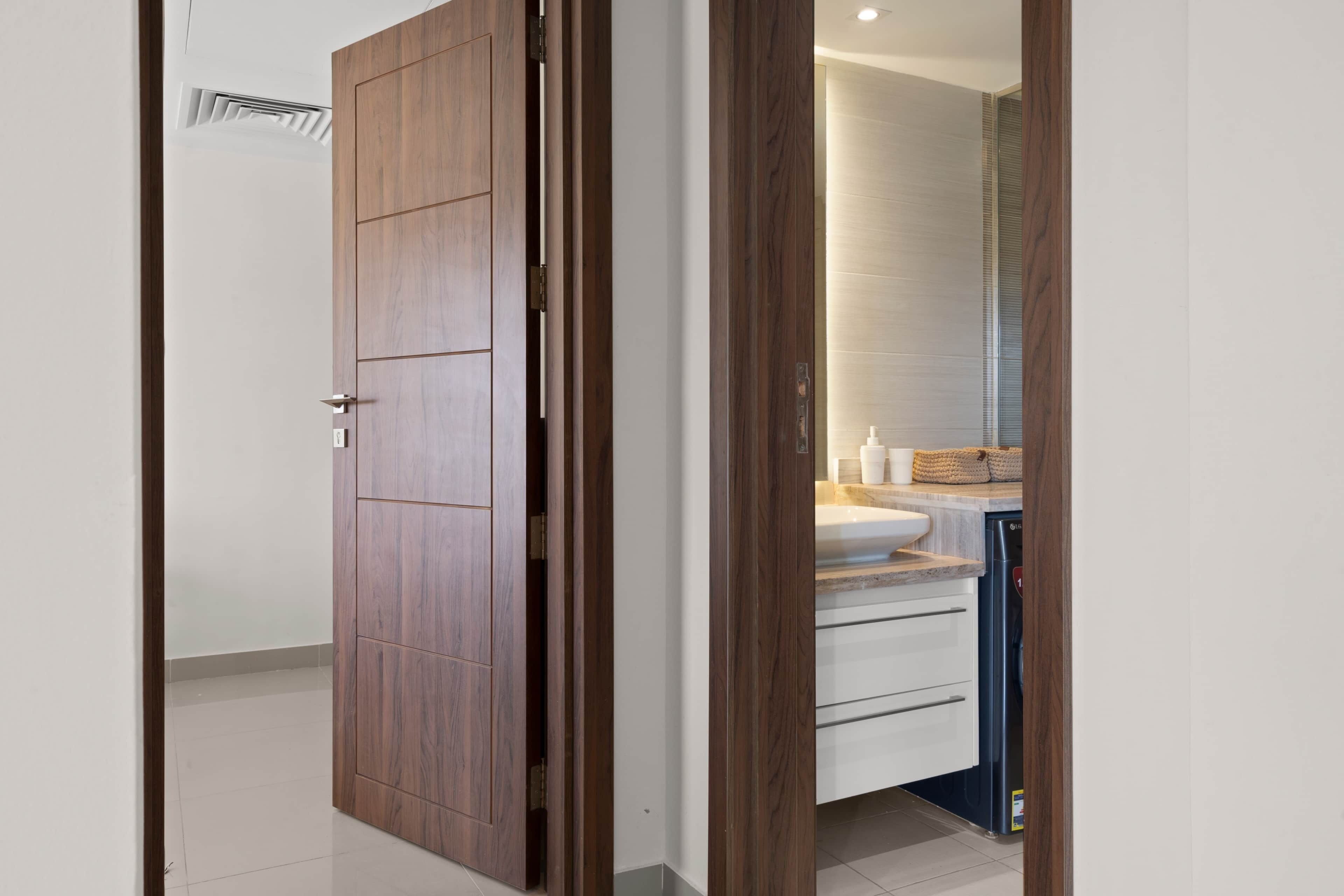 Una puerta de madera que da a un baño con lavabo, encimera y espejo.