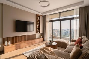 Un salon moderne doté d’un téléviseur à écran plat, d’une console en bois, d’une table basse ronde et d’un canapé agrémenté de coussins.
