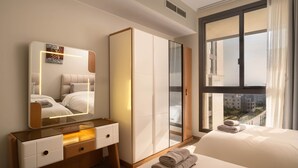 A hotel room with a bed, a bedside table with a mirror, a wardrobe, and a view of buildings through a large window. - AEON Towers Lucky Cloud #606 - nesty (6th of October City)