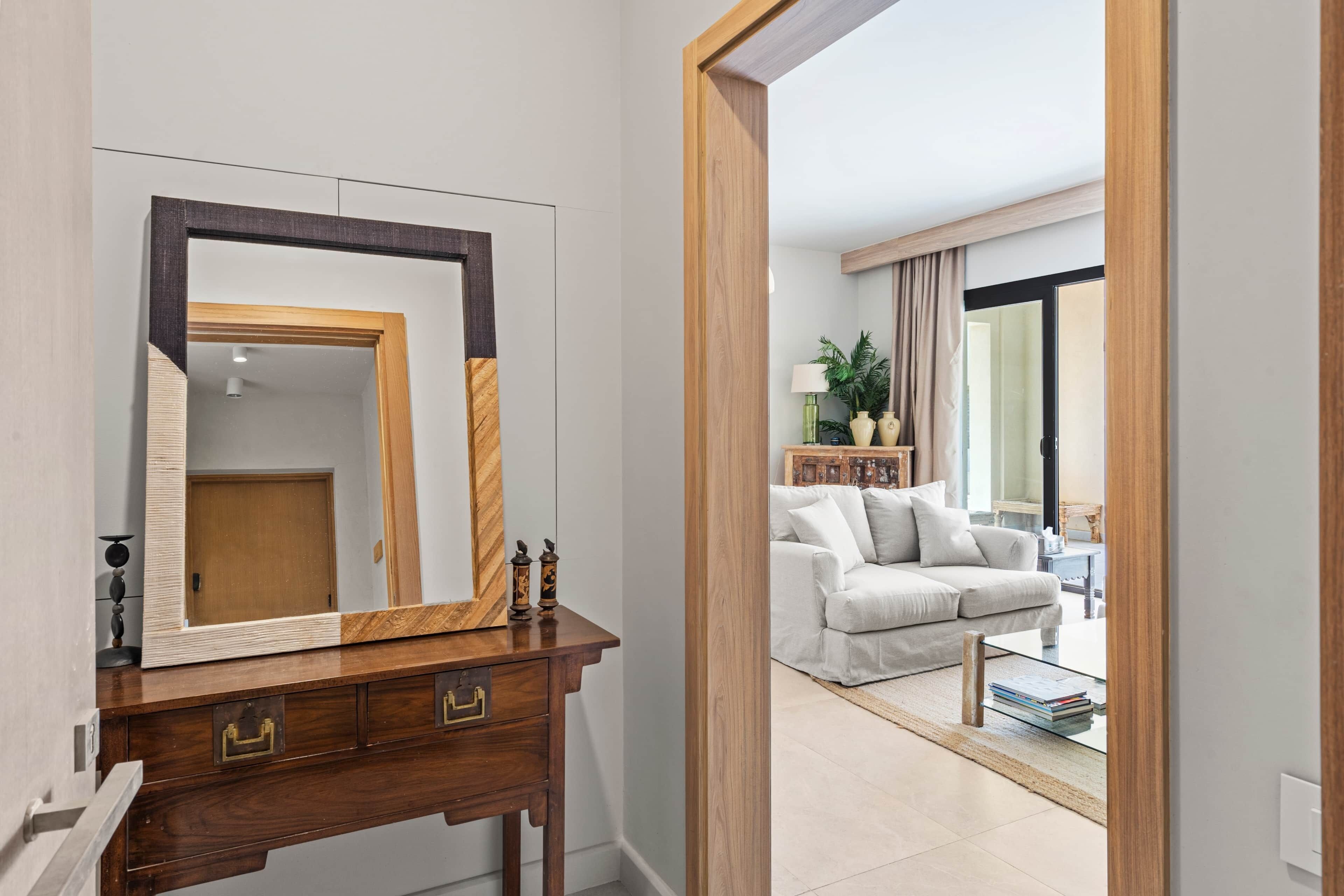 Una habitación con un aparador de madera, un espejo grande, un sofá blanco y una mesa de centro.