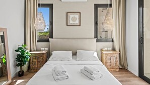 Ein modernes Schlafzimmer mit einem großen Bett, zwei Nachttischen, einer Topfpflanze und Blick ins Freie.