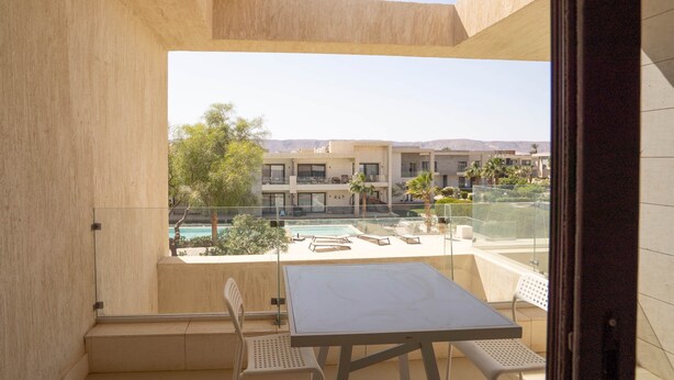A balcony with a table and chairs, overlooking a pool and buildings.
