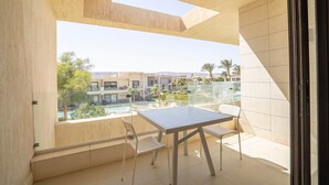 A balcony with a table and chairs, a glass railing, and a view of buildings and greenery.