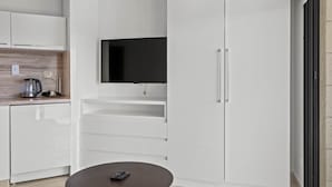 A modern kitchen with white cabinetry, a flat-screen TV mounted above the countertop, and a coffee maker on the counter.
