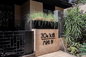 Une entrée d’immeuble avec une plaque indiquant « 20c St.18 MRG N » et un bac à fleurs contenant de l’herbe.