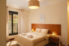 Une chambre d’hôtel comprenant un lit, une table de chevet avec une lampe, une fenêtre avec des rideaux et une œuvre d’art accrochée au mur.