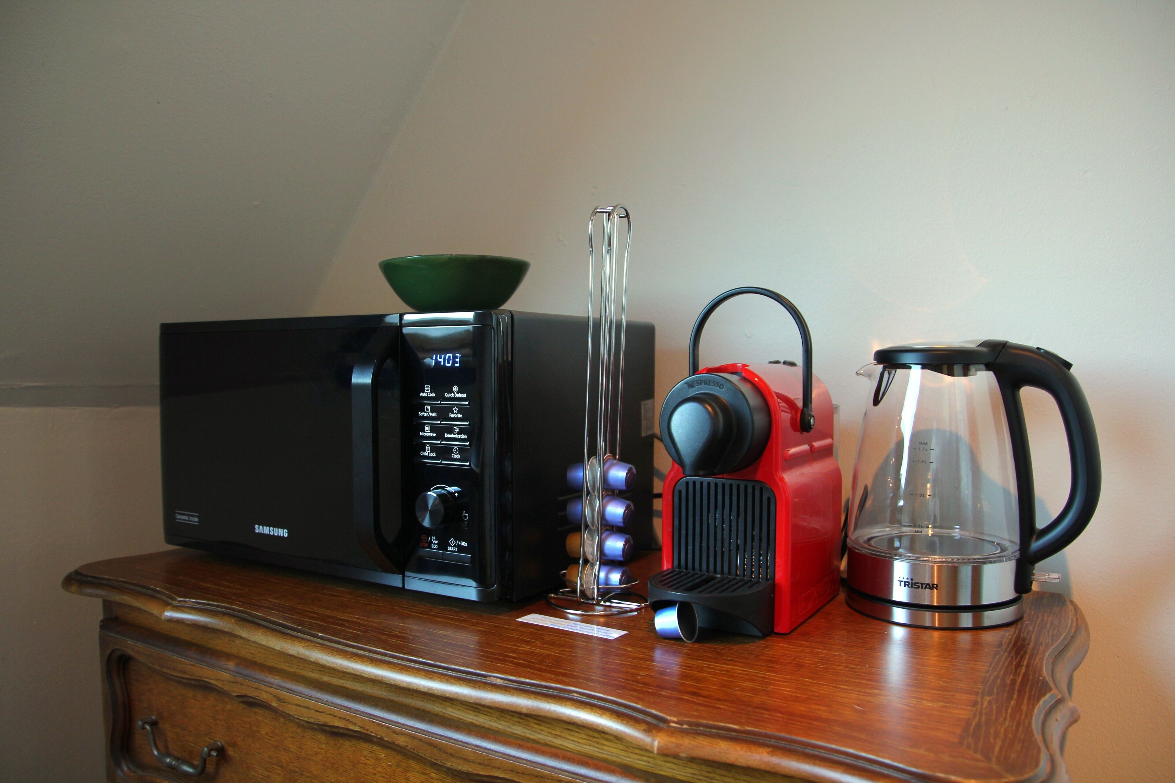 Una cocina con microondas, cafetera y hervidor sobre un mueble de madera.