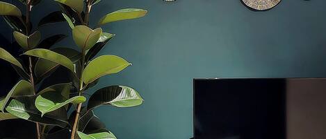 Una sala de estar con una planta en maceta, un televisor de pantalla plana, decoración en la pared y un mueble.