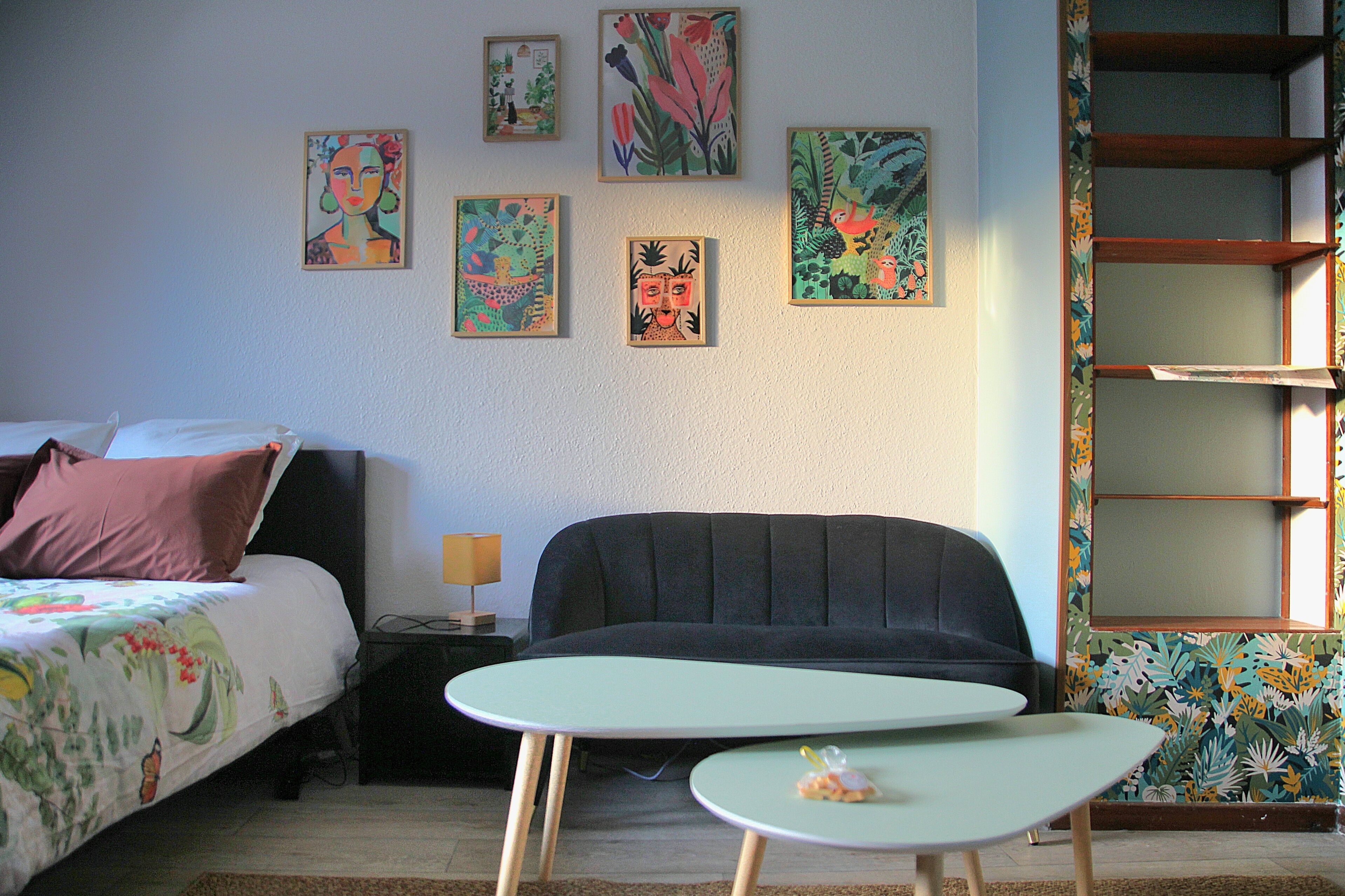 A bedroom with a bed, a sofa, a small table, and a wall with artwork.