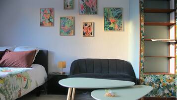 A bedroom with a bed, a sofa, a small table, and a wall with artwork.